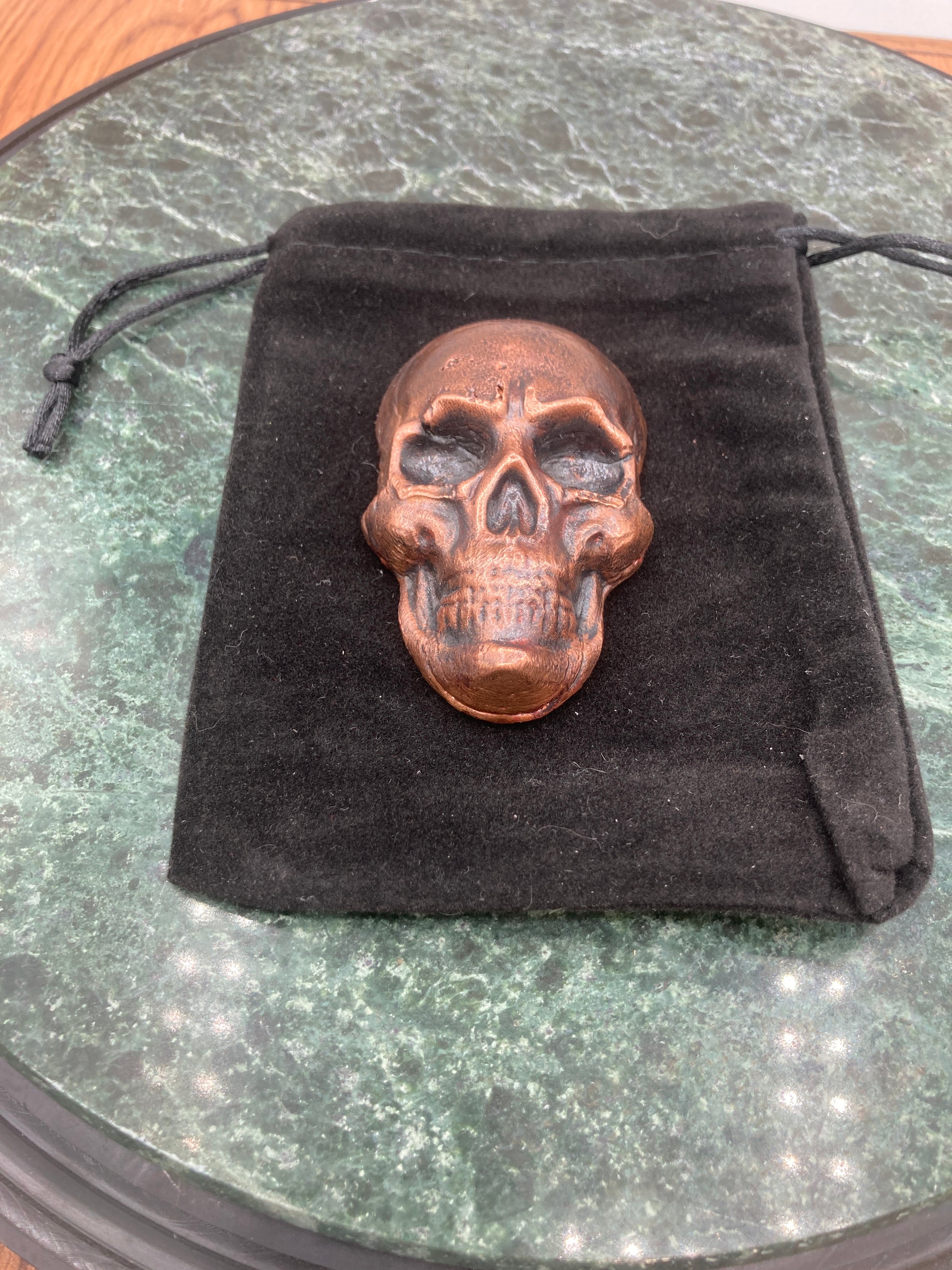 Bronze skull pendant on a black cloth with a reflective surface background