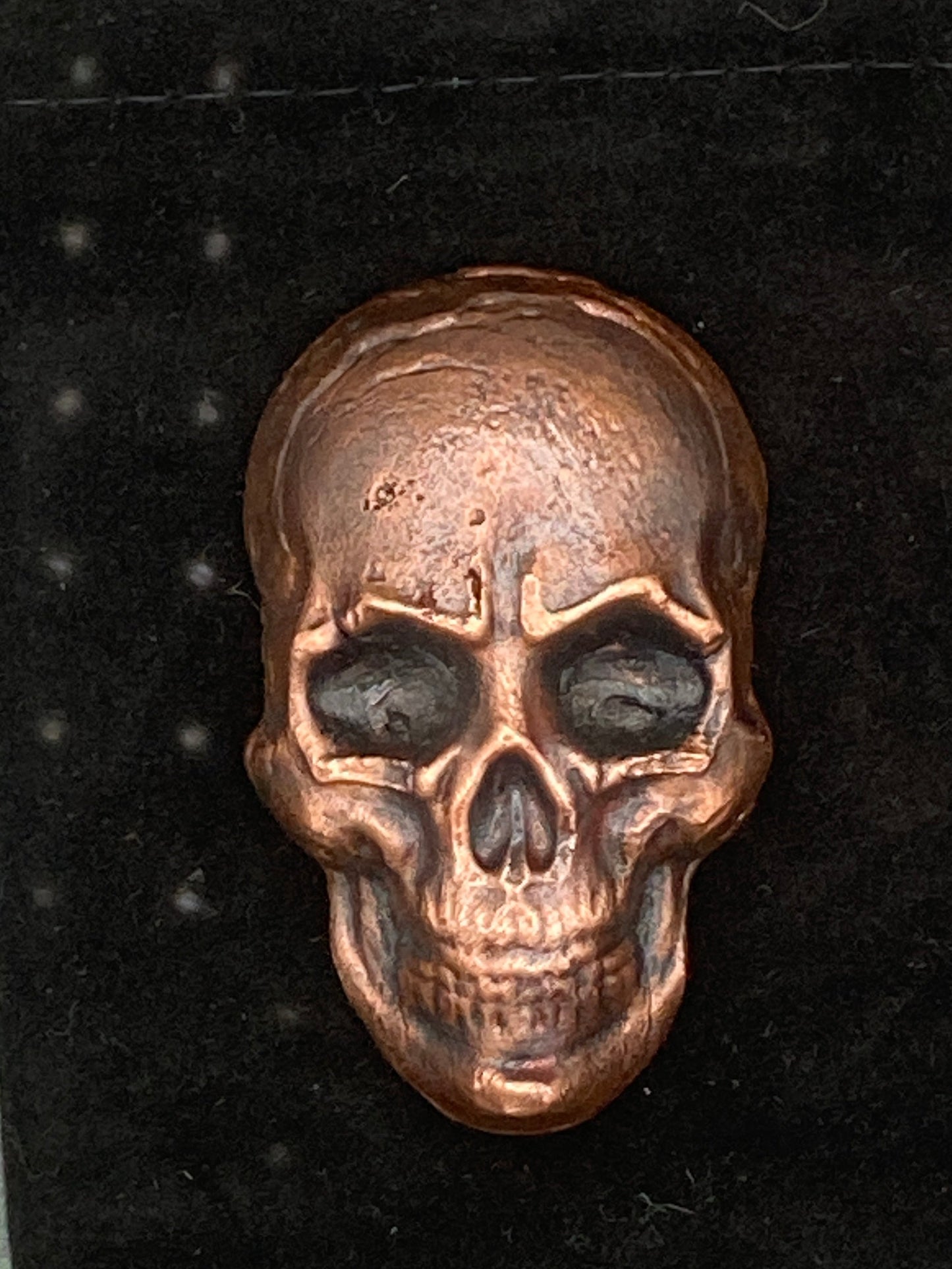 Bronze skull-shaped object on a black velvet cushion with a gray textured background