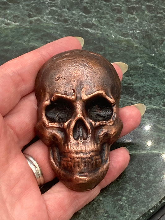 Bronze skull-shaped object held in a hand against a green marble background