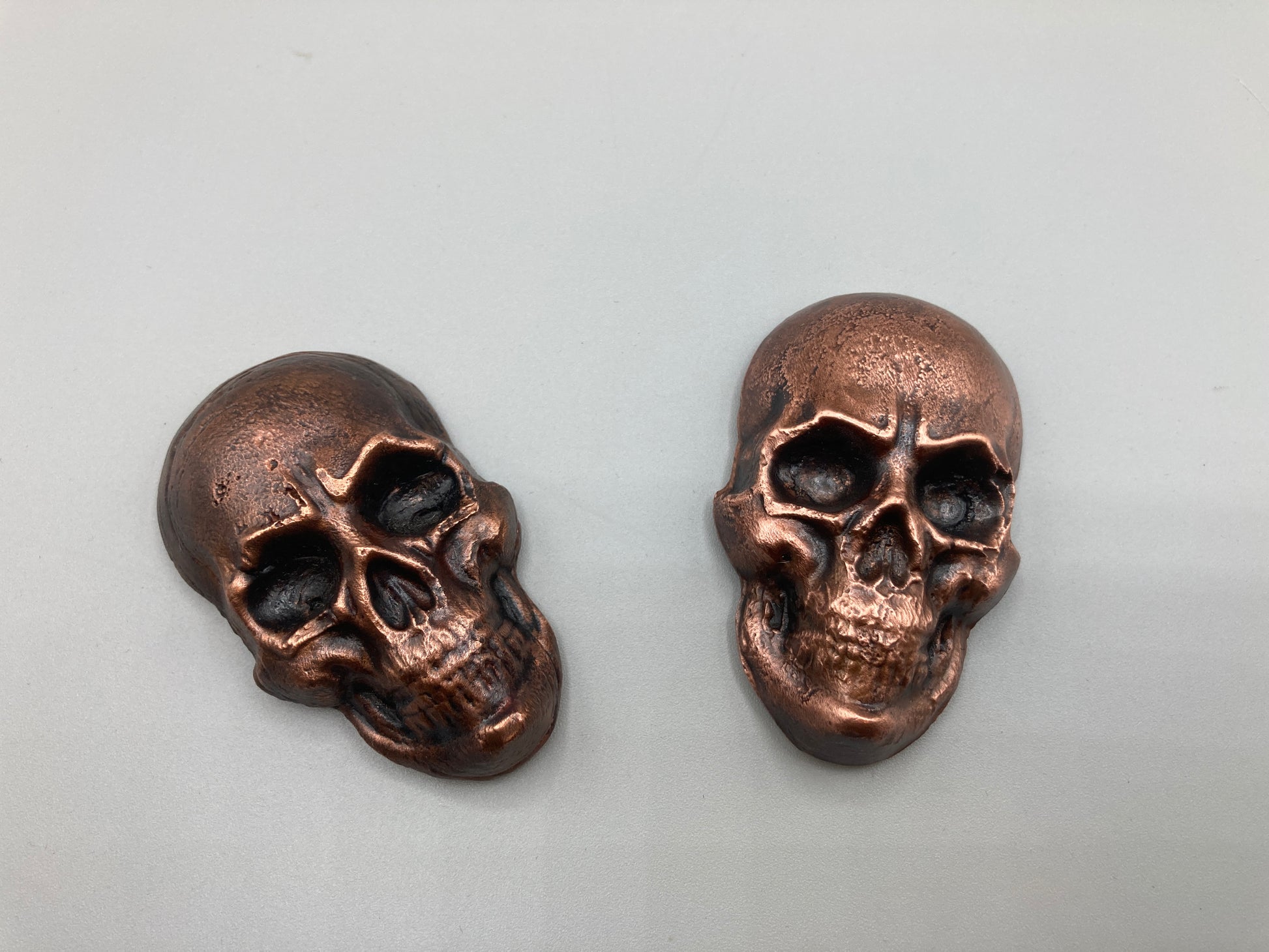 Two bronze skull-shaped objects on a light gray background