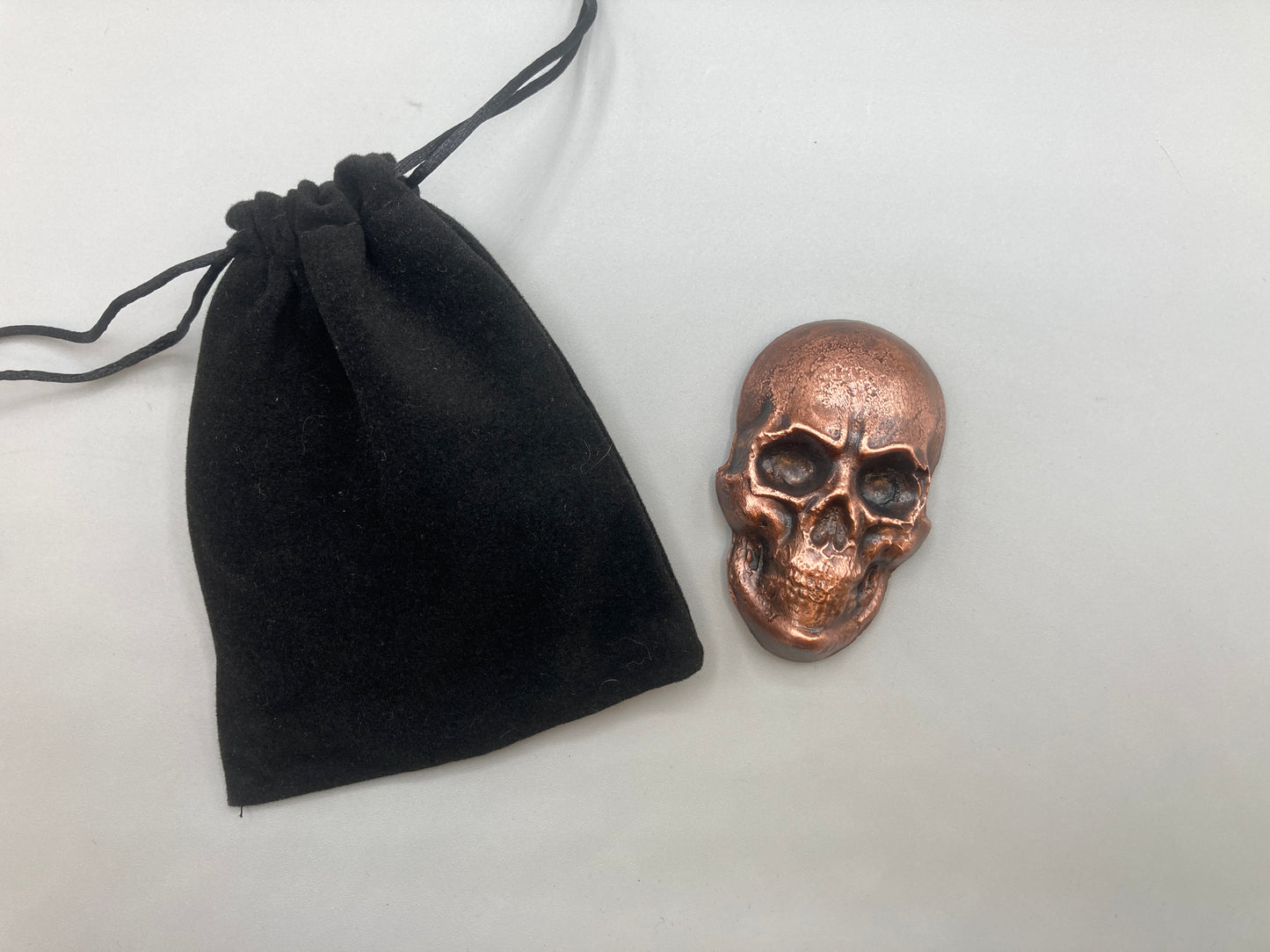 Bronze skull-shaped object next to a black drawstring bag on a light gray background