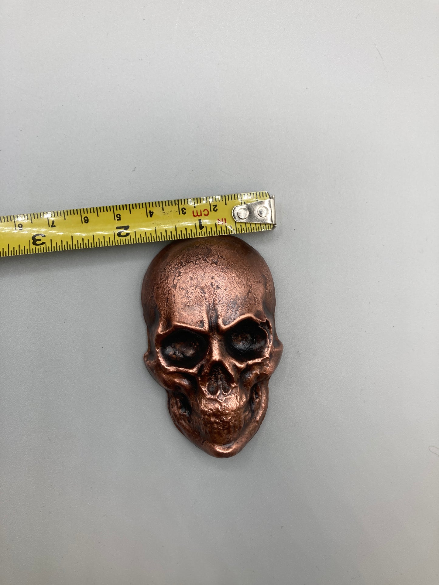 Bronze skull-shaped object with a measuring tape for scale on a gray background