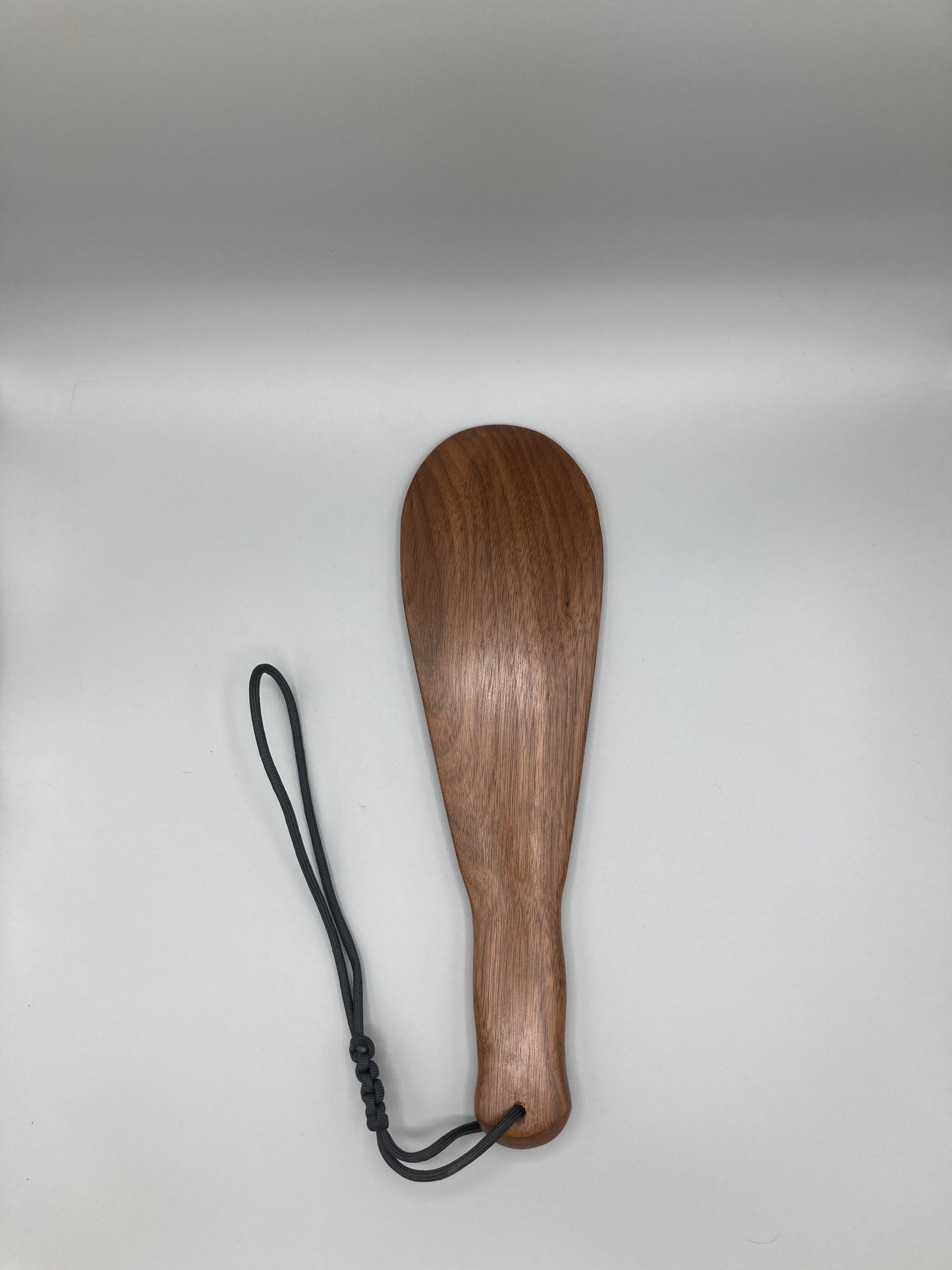 Wooden paddle with a black strap on a light gray background